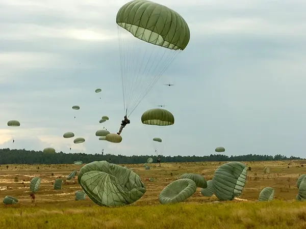 Military paratroopers with green parachutes descending into a field, representing the historic D-Day airborne assault in Normandy, a key narrative explored on our WW2 battlefield tours.