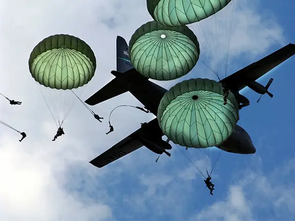 Silhouettes of military paratroopers jumping from a transport aircraft against a cloudy sky, symbolizing the airborne operations of D-Day featured on our WW2 Normandy battlefield tours.