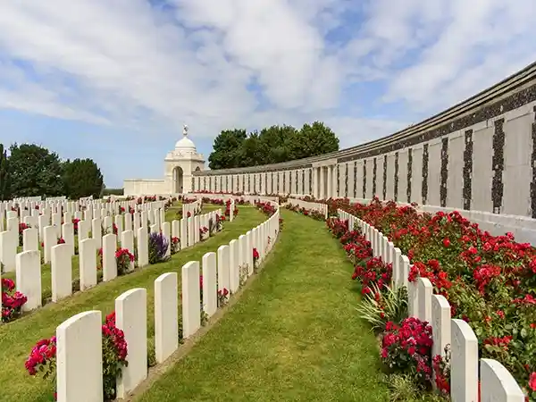 Rows of white headstones and blooming red roses along the curved memorial wall at Tyne Cot Cemetery, a deeply moving site visited on our WW1 Flanders and Somme battlefield tours.